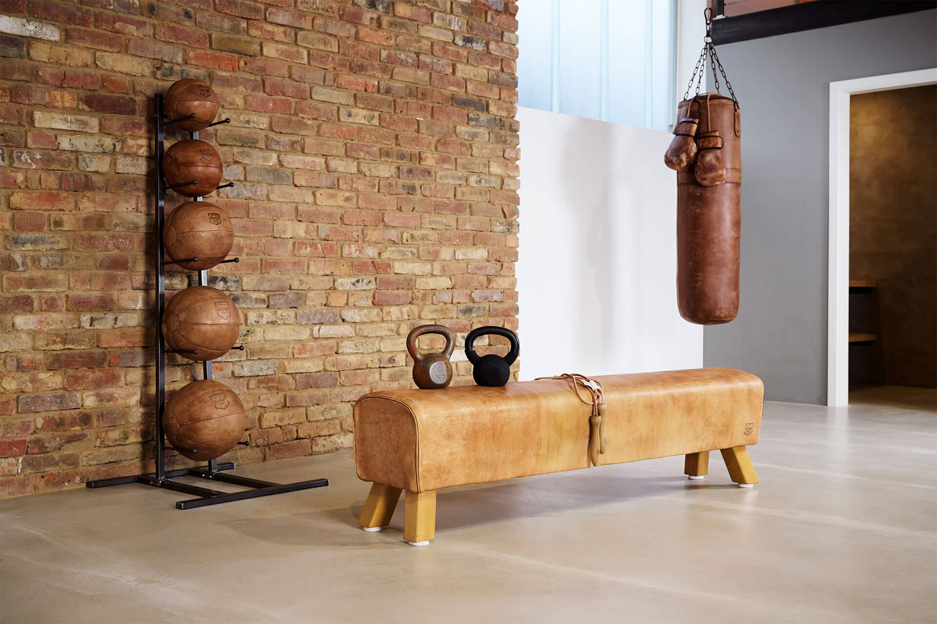 ARTZT Vintage Medizinbälle, Pferd und Boxsack befinden sich in einem Raum vor einer Ziegelwand.